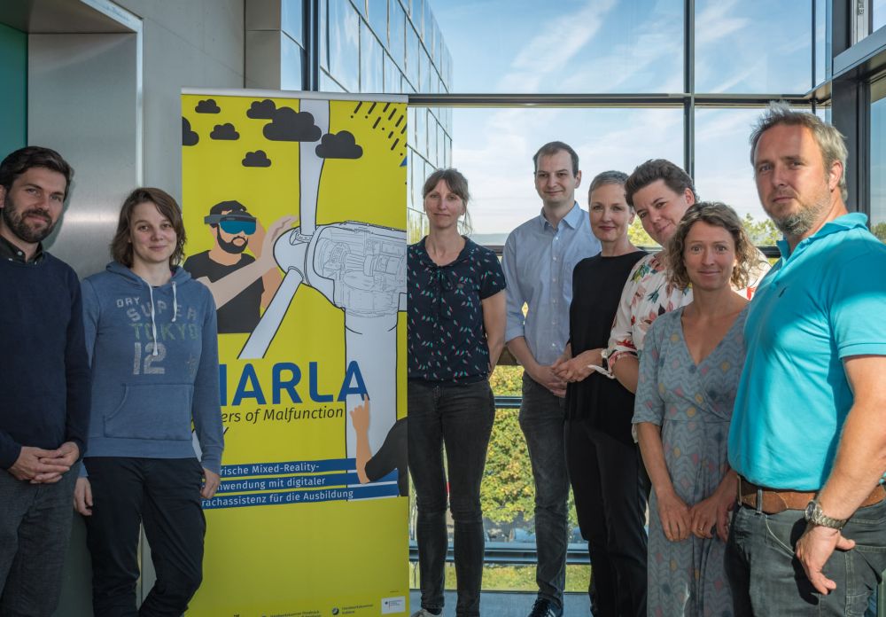 © MARLA-Projekt MARLA-Projektteam mit Plakat, auf dem ein Windrad und ein Mann mit einer VR-Brille zu sehen ist.