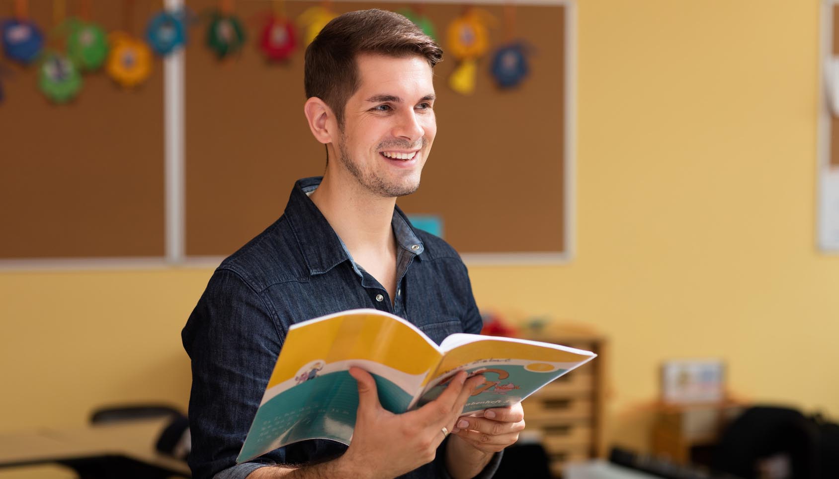 © Christian Schwier/Fotolia Lehrer mit Schulheft in der Hand steht im Klassenzimmer vor einer Tafel